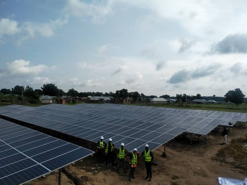 Solar panels covering a massive area and four workers standing in front of the first-row panels