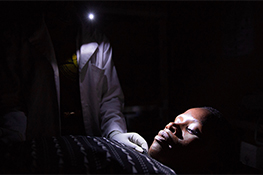 Tanzania midwife at night holding cell phone in mouth. Photo credit: We Care Solar