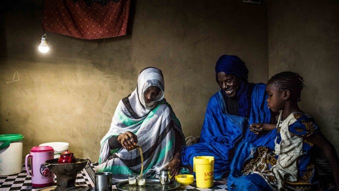 Two African women and a young child sharing a meal under the light of a solar lamp