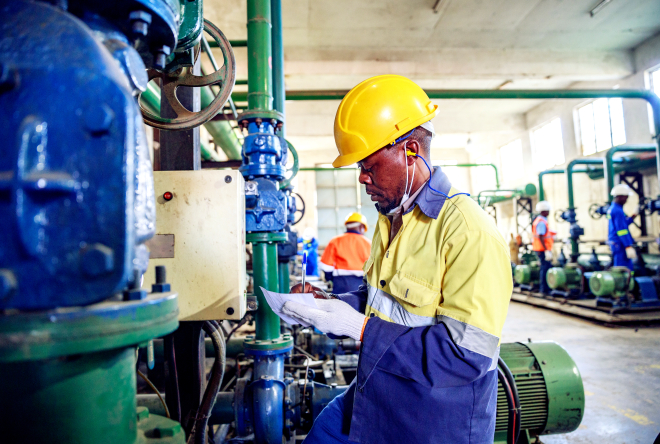 Worker inspecting industrial equipment and recording data inside a pump facility.