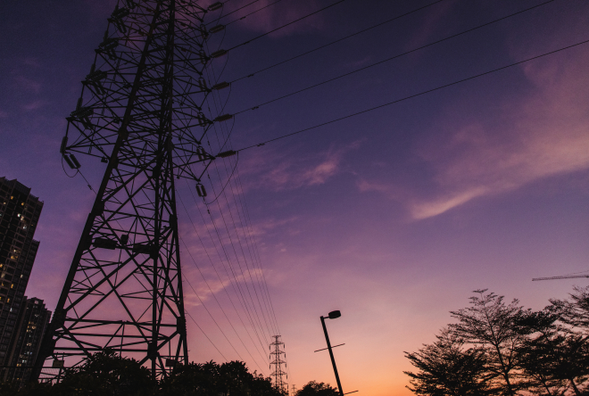 High-voltage transmission towers and power lines silhouetted against a purple and orange sunset sky.