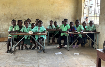 Three children sit outdoors, learning together while looking at a laptop.
