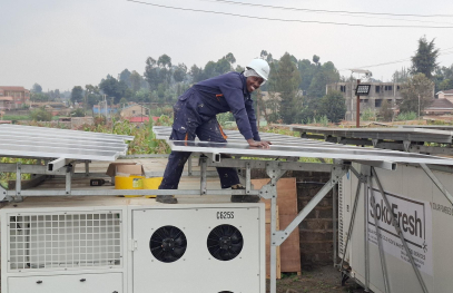 A technician installs solar panels on a rooftop system connected to refrigeration units