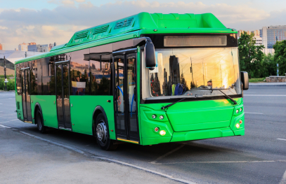 A modern green electric city bus parked on a street at sunset