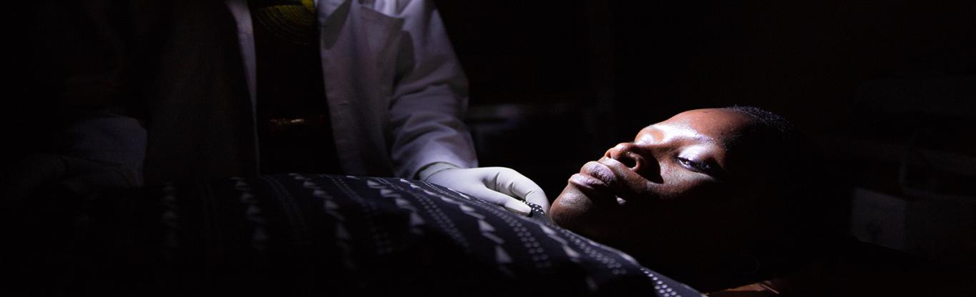 Tanzania midwife at night holding cell phone in mouth. Photo credit: We Care Solar