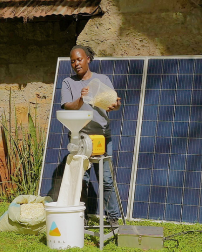 Energy Access - Banner A person operates a grain milling machine powered by solar panels installed outdoors, with two large solar panels positioned behind the equipment.