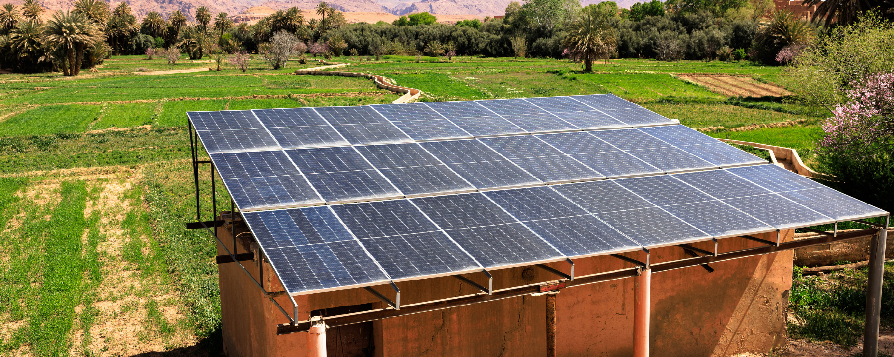 Solar panels mounted on the roof of a small building in a rural setting, with trees and open land visible around the structure.