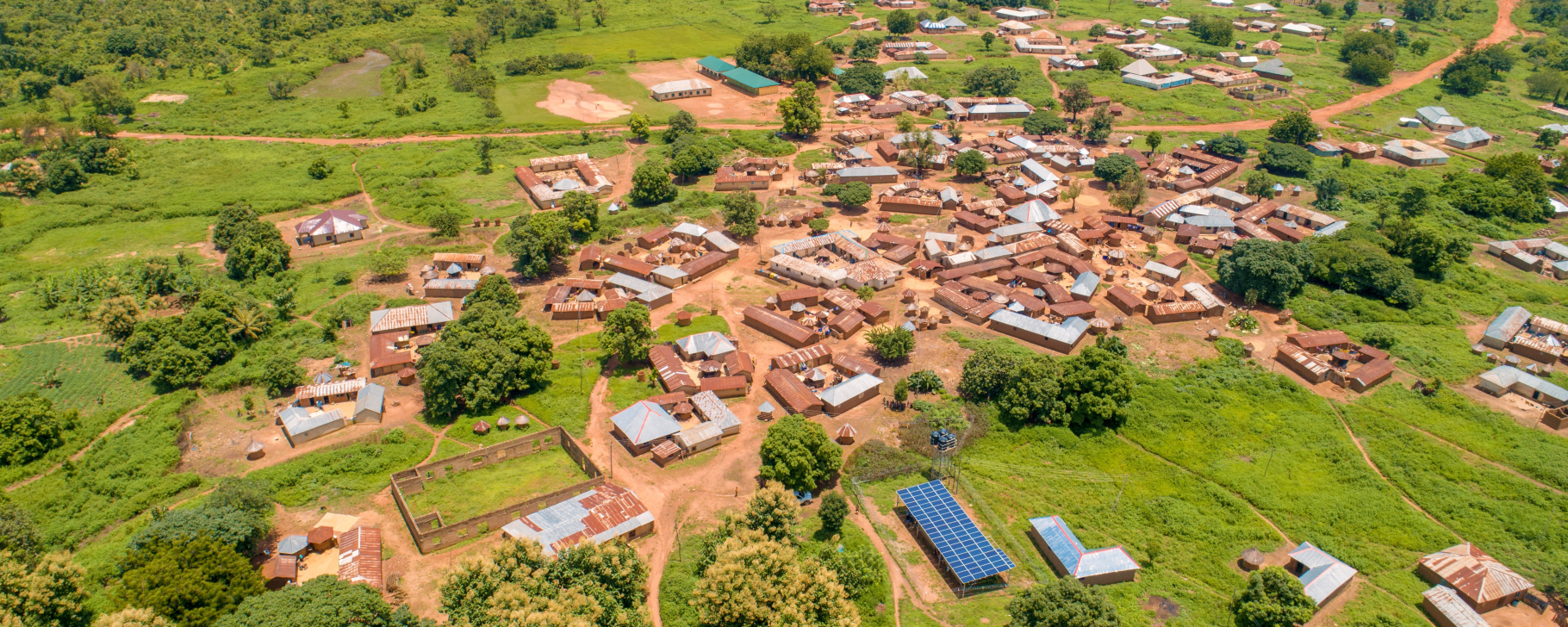 Aerial view of a rural community surrounded by greenery, with homes, roads, and a solar-powered mini-grid installation visible near the village center.