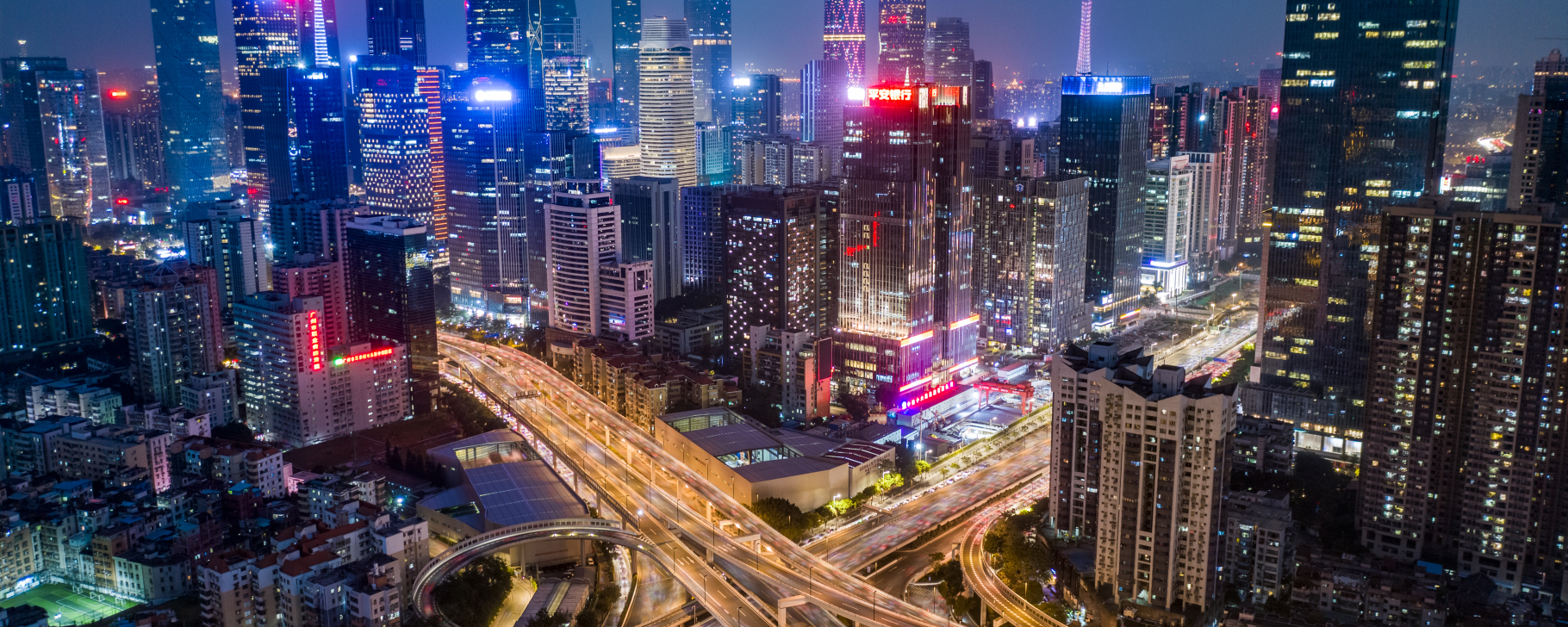 Nighttime city skyline with illuminated skyscrapers and elevated highways weaving through downtown.