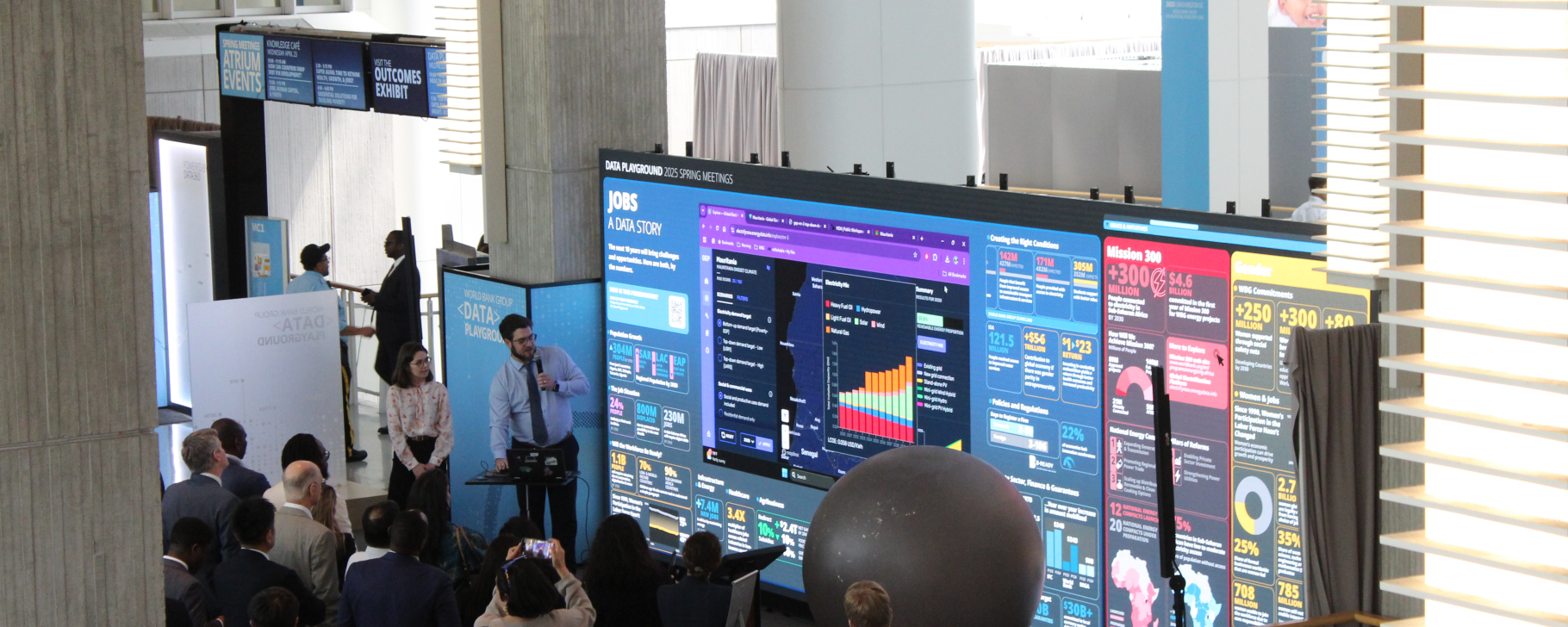 People gathered at a conference booth with a large digital display and city skyline backdrop.