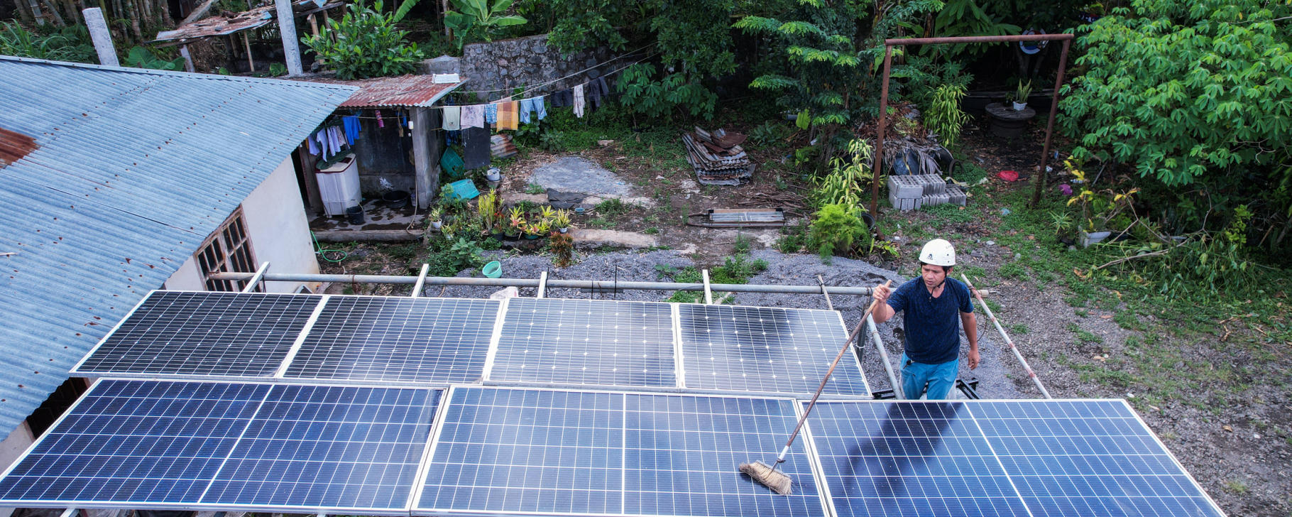 Access to Electricity Rooftop solar panels installed at a home, with a worker cleaning panels in a rural setting.
