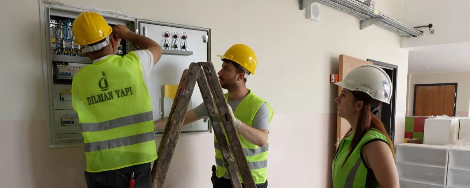 Construction worker performing electrical work on a distribution panel inside a building