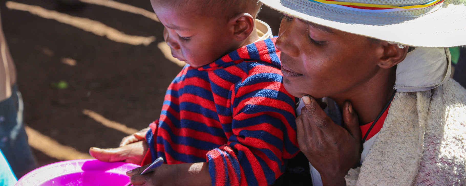African woman with a hat holding a child in her lap who is eating