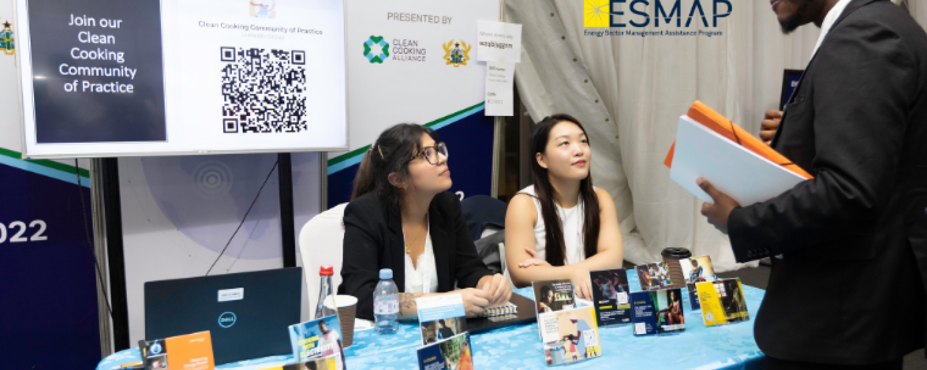 Two young women and a man at a booth at a knowledge exchange event hosted by ESMAP