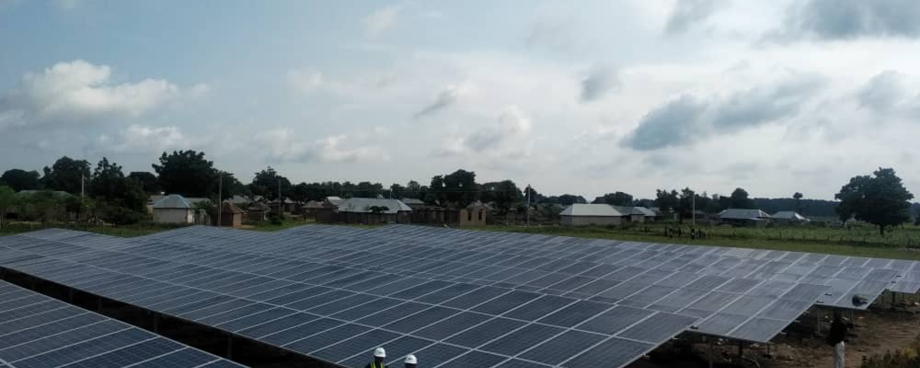 Climate finance for solar and wind Massive area covered with solar panels and four workers standing in front of them