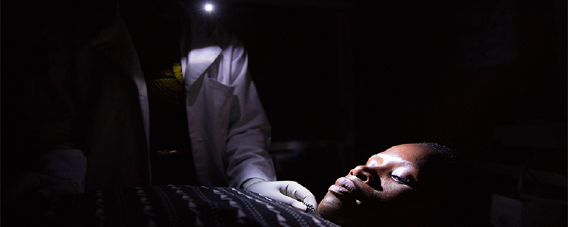 Tanzania midwife at night holding cell phone in mouth, Photo credit: We Care Solar