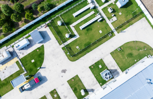 Aerial view of an industrial energy facility with buildings, pipelines, tanks, and service roads arranged on landscaped grounds.