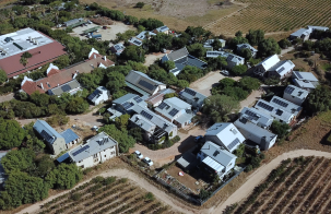 Aerial view of a rural village with homes, many with rooftop solar panels, surrounded by fields and greenery.