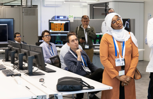 Participants visiting a control room, listening to a presentation beside computer workstations and monitoring screens.