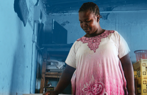 Woman standing in a kitchen with walls painted blue using an electric cooker