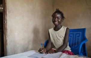 Young child smiles while sitting at a desk and writing in a notebook