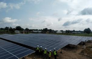 Climate finance for solar and wind Solar panels covering a massive area and four workers standing in front of the first-row panels