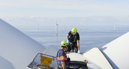 Credit: Ørsted Technicians work atop an offshore wind turbine, with wind turbines visible across the sea.