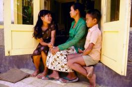 mother and children sitting in front of their home