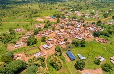 Aerial view of a rural community surrounded by greenery, with homes, roads, and a solar-powered mini-grid installation visible near the village center.