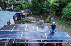 Rooftop solar panels installed at a home, with a worker cleaning panels in a rural setting.