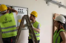 Construction worker performing electrical work on a distribution panel inside a building