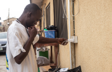 Person connects a charger to a wall socket while standing outside a residential building